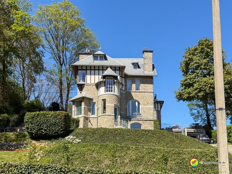 Villa mit Fachwerk und Erker hinter einer hohen Hecke.