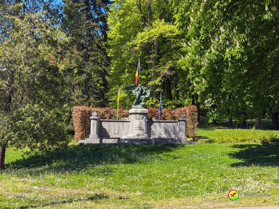 Kriegerdenkmal mit belgischer und wallonischer Fahne in einer Parkanlage.