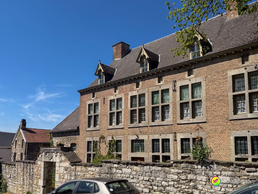 Langes Backsteingebäude mit vielen Fenstern über einer Bruchsteinmauer.