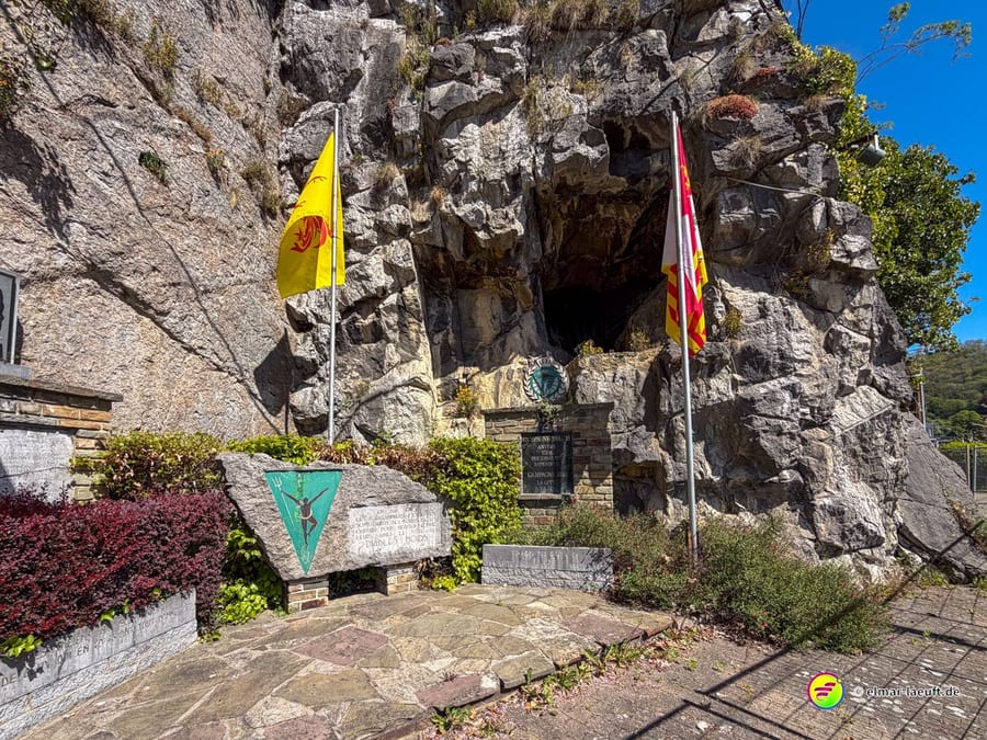 Felswand mit Grotte, davor Fahnen und Gedenktafeln.