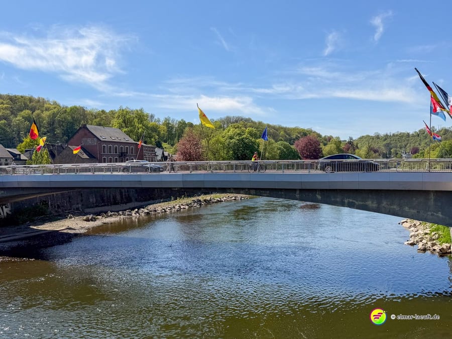 Moderne Brücke über den Fluss, am Geländer bunte Fahnen.