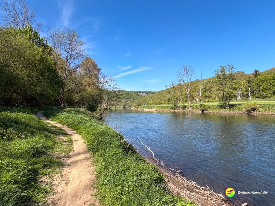 Sandiger Uferpfad dicht am Wasser, gegenüber eine grüne Wiese.