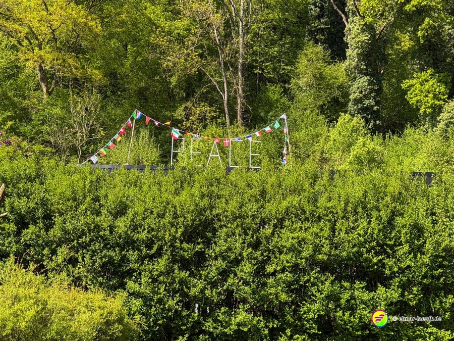Große weiße Buchstaben PEACE im Grün, darüber eine Kette bunter Wimpel.