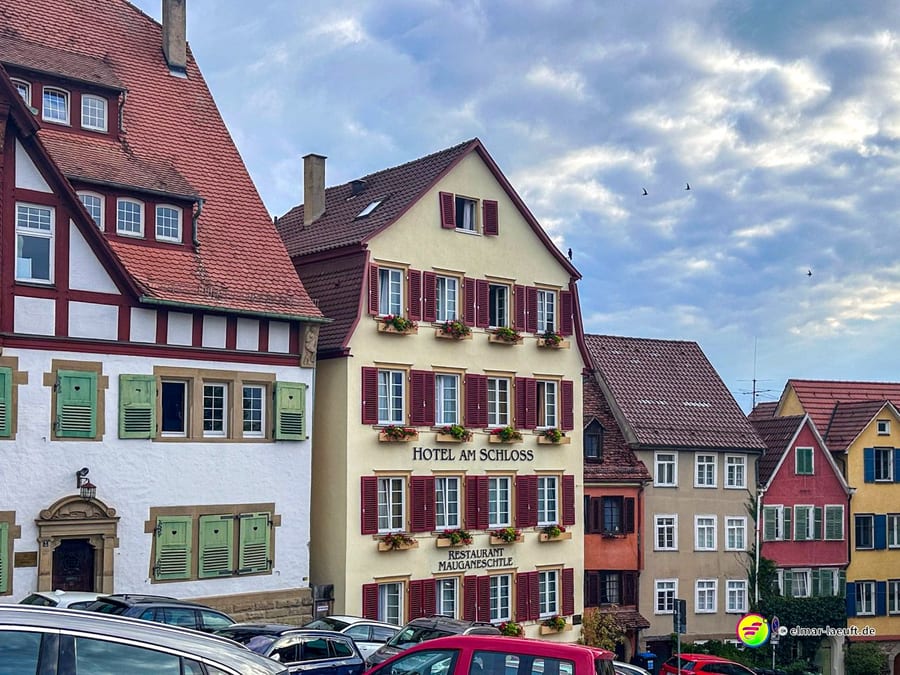 Laufen durch die historische Altstadt von Tübingen mit Fachwerkhäusern und einem Hotel am Schloss bei bewölktem Himmel.