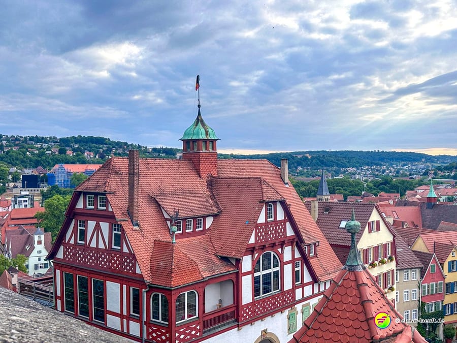 Laufen in Tübingen mit Blick auf historische Fachwerkhäuser und die grüne Hügellandschaft im Hintergrund unter einem bewölkten Himmel.