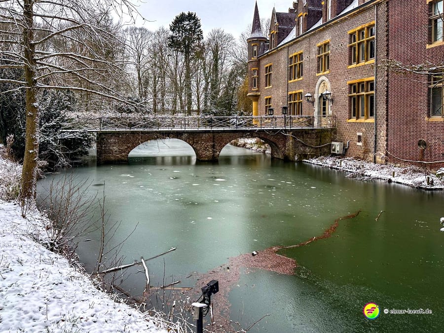 Laufen im winterlichen Heerlen entlang eines zugefrorenen Gewässers mit einer alten Brücke und einem historischen Backsteingebäude.