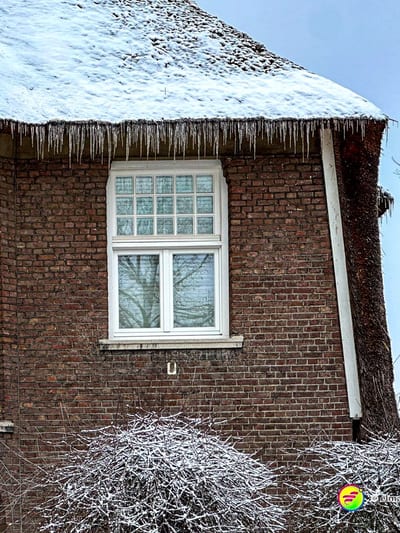 Laufen in Heerlen an einem winterlichen Tag mit schneebedecktem Reetdach und Eiszapfen an einem Backsteinhaus.