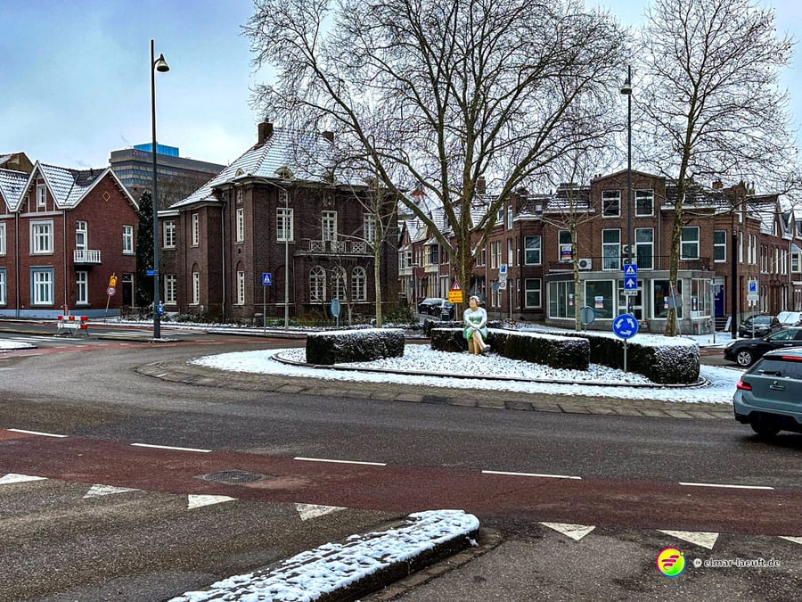 Laufen durch eine verschneite Stadt mit alten Backsteinhäusern und einem kleinen Kreisverkehr mit einer sitzenden Skulptur in Heerlen.