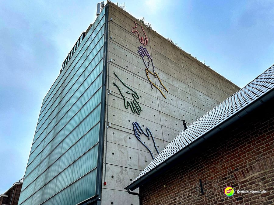 Laufen in Heerlen vorbei an einem modernen Gebäude mit bunter Handkunst an der Fassade und einem schneebedeckten Dach im Vordergrund.