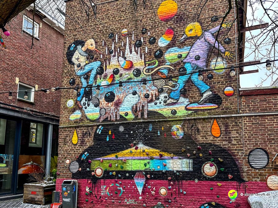 Laufen in Heerlen führt an einer bunten, fantasievollen Wandmalerei vorbei, die zwei Figuren und viele bunte Kugeln auf einer Backsteinmauer zeigt.