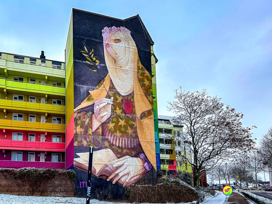 Laufen in Heerlen an einem winterlichen Tag vorbei an einem bunten Wohnhaus mit großem Wandgemälde einer Frau mit Buch und Olivenzweig.