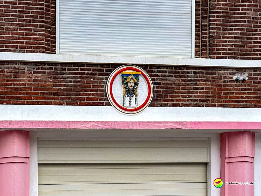 Beim Laufen in Heerlen fällt eine bunte, runde Wanddekoration mit einem Frauenkopf an einem Backsteinhaus auf.