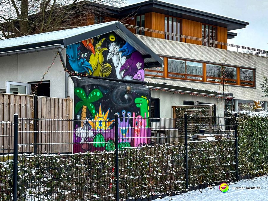 Beim Laufen in Heerlen zeigt sich ein buntes Graffiti an einem Haus mit winterlicher Schneedecke auf dem Zaun und Boden.
