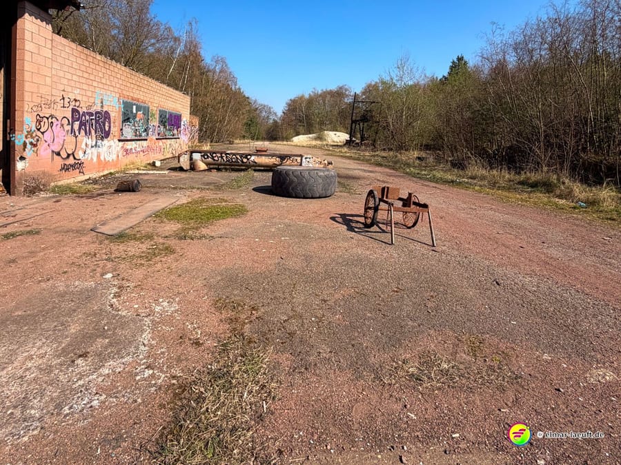 Laufen auf einem verlassenen, mit Graffiti bedeckten Industrieareal in Maasmechelen mit alten Reifen und Metallgestellen auf dem Weg unter blauem Himmel.