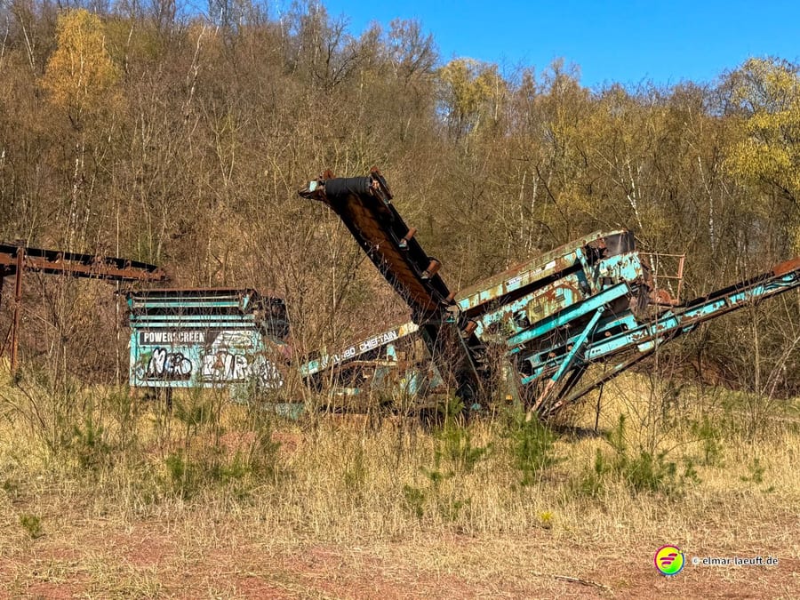 Beim Laufen in Maasmechelen führt der Weg an einer verlassenen, rostigen Förderanlage vorbei, umgeben von trockenem Gras und kahlen Bäumen.